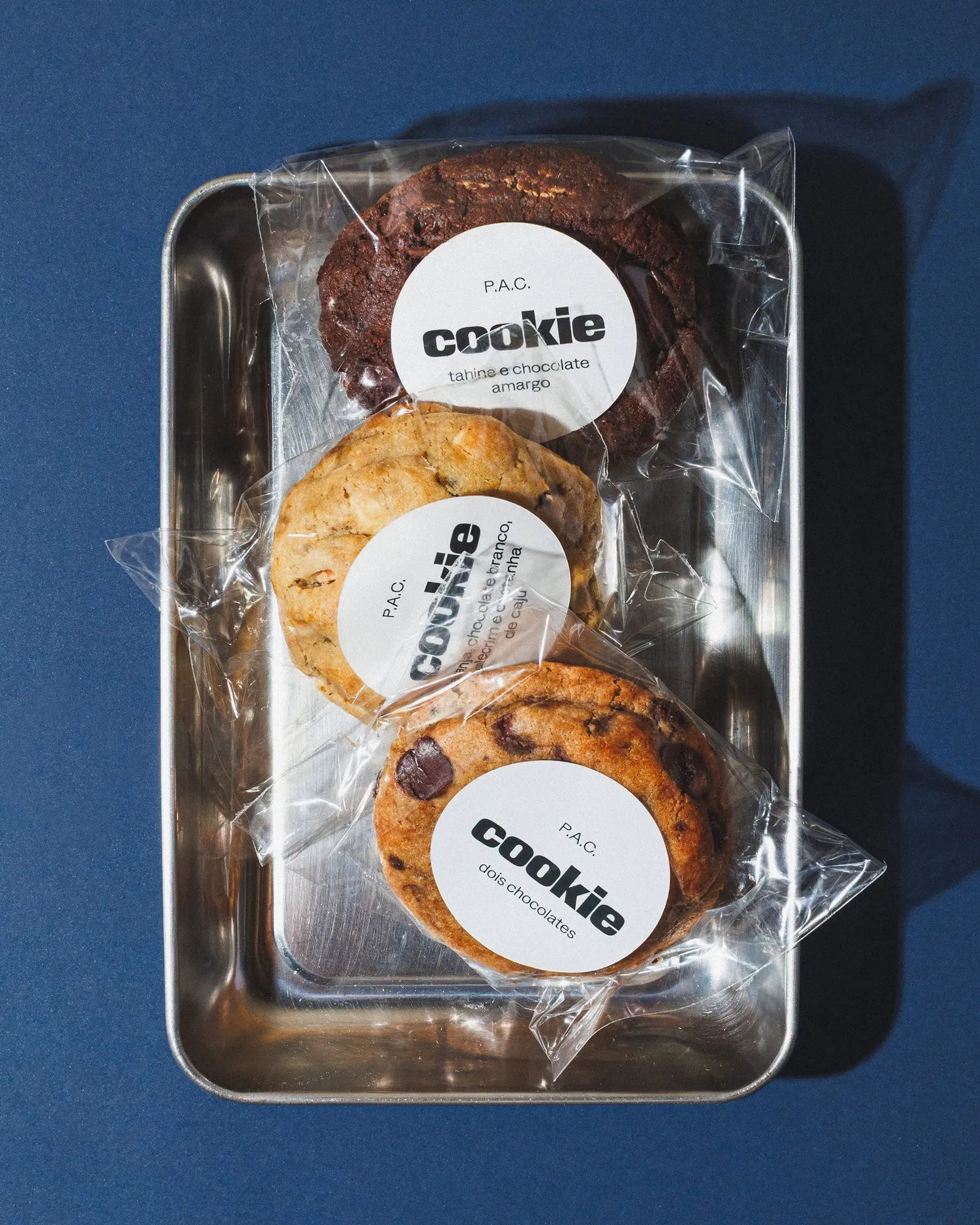 Bandeja con tres galletas envueltas en plástico transparente y etiquetas que dicen «cookie», sobre fondo azul