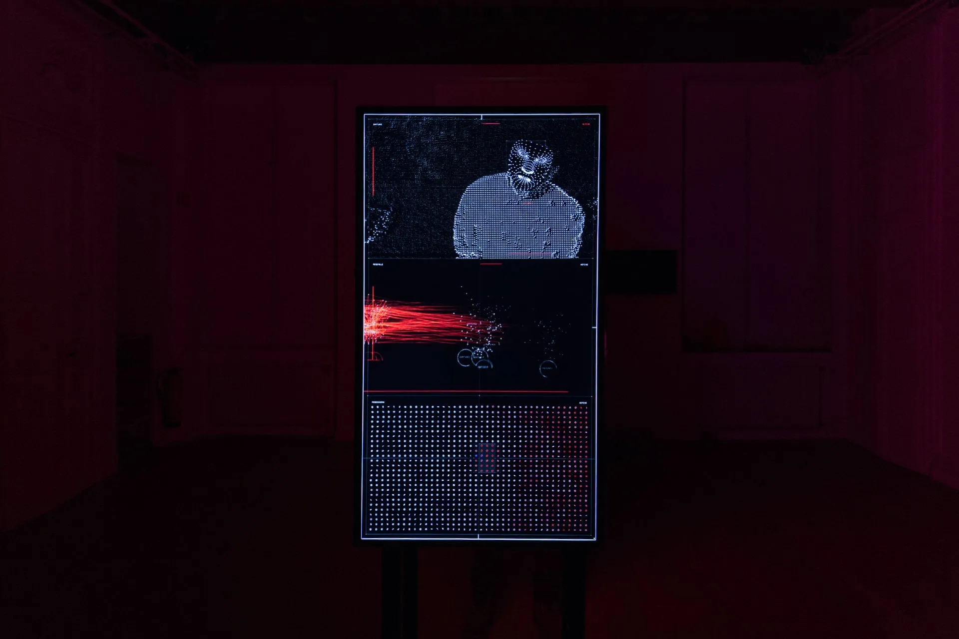 Pantalla de datos de la escultura en una sala vacía, con la imagen del visitante troceada y una nube de partículas rojas