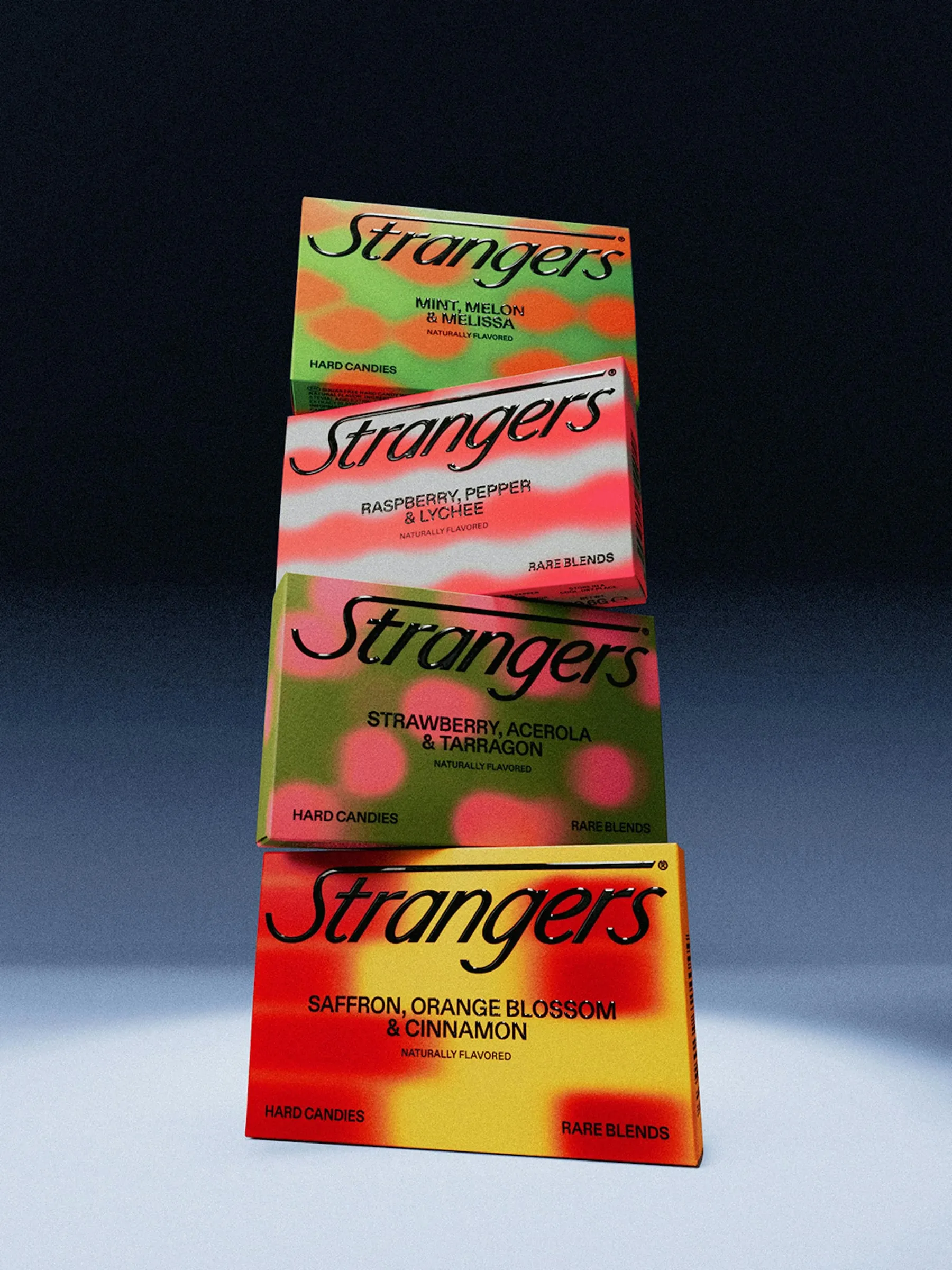 Torre de cuatro cajas de caramelos Strangers apiladas ligeramente torcidas, con estampados rojos, rosas, verdes y amarillos sobre fondo azul oscuro