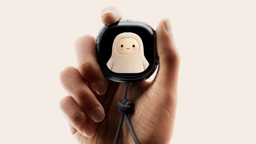 Una mano sostiene el Muse Charm de Meta, un dispositivo colgante con pantalla negra que muestra un pequeño personaje peludo de color crema