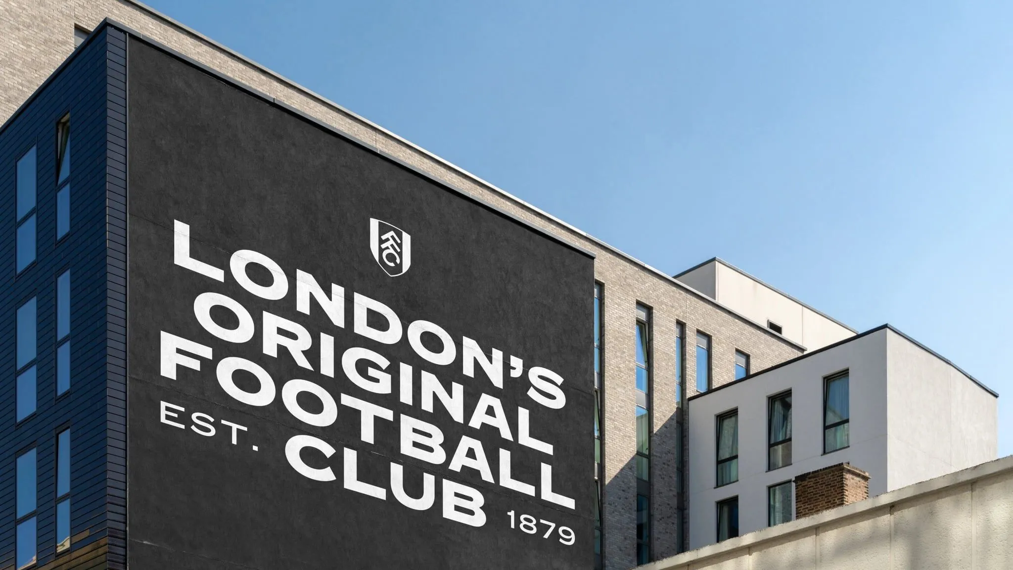 Mural negro en la fachada de un edificio de ladrillo con las letras blancas inclinadas «London's Original Football Club Est. 1879» y el escudo del Fulham