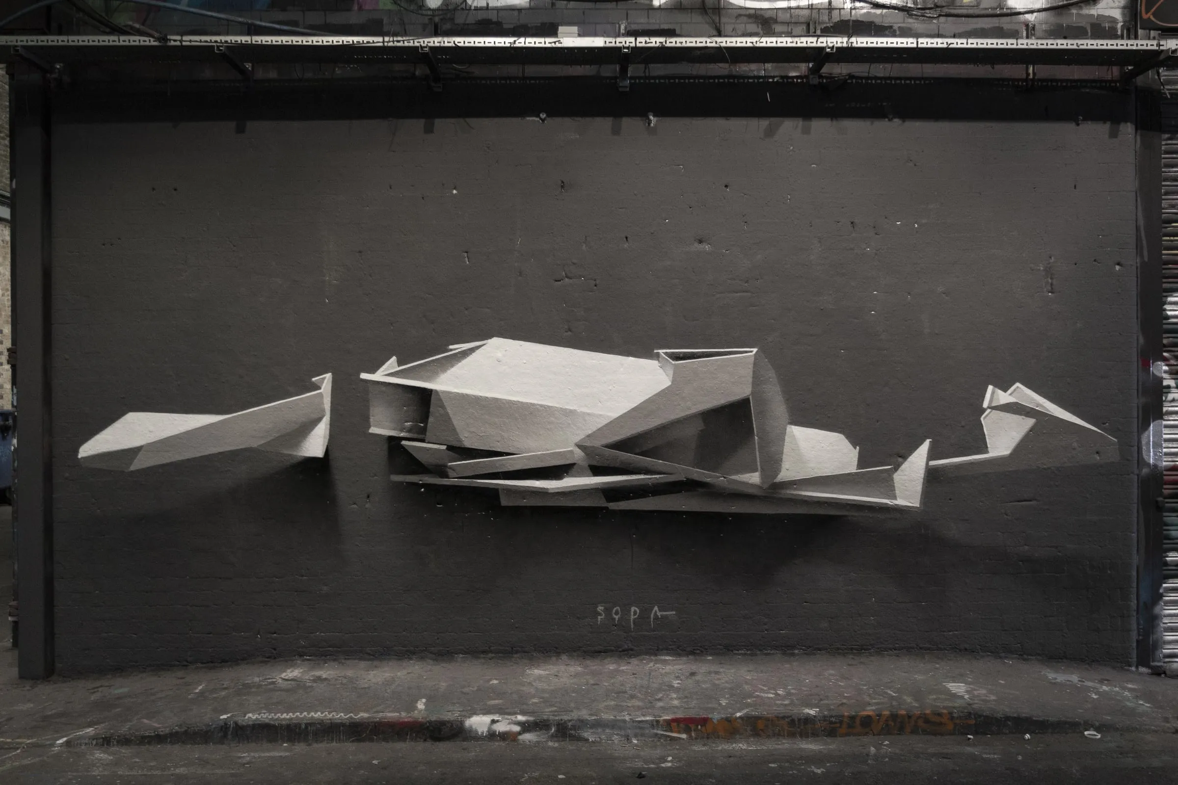 Muro negro con una escultura de piezas geométricas grises y blancas que parece flotar delante de la pared y forma las letras de SODA