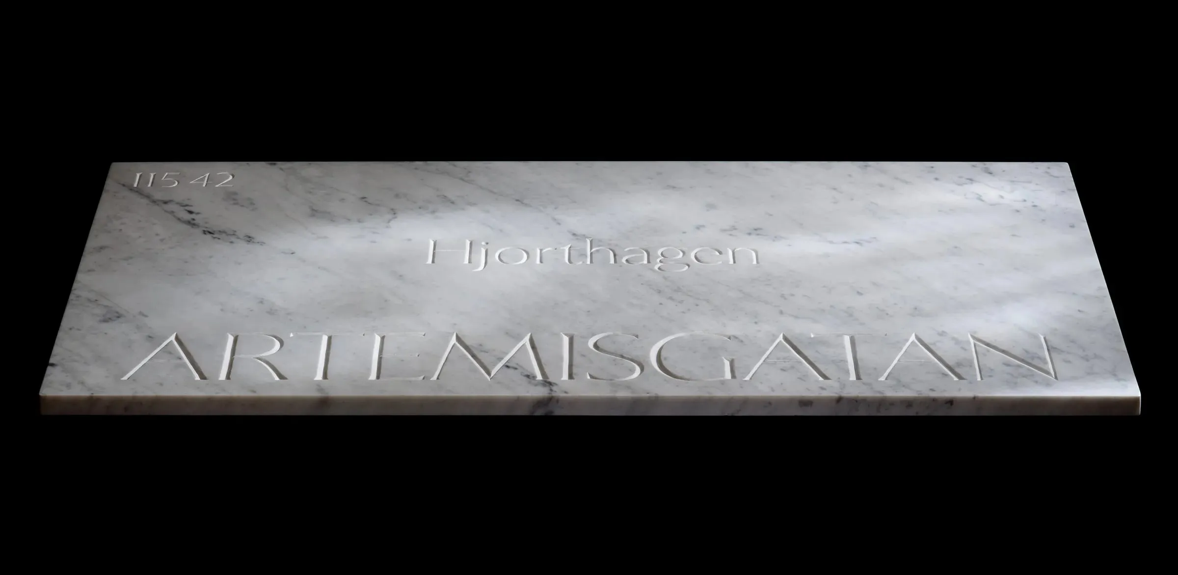 Placa de mármol blanco veteado tallada con las palabras «Hjorthagen» y «Artemisgatan», fotografiada en ángulo