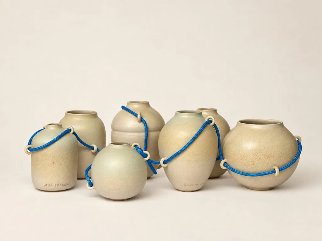 Seis vasijas de gres en tonos crema y verde, unidas entre sí por un cordón azul que pasa por pequeñas asas cerámicas
