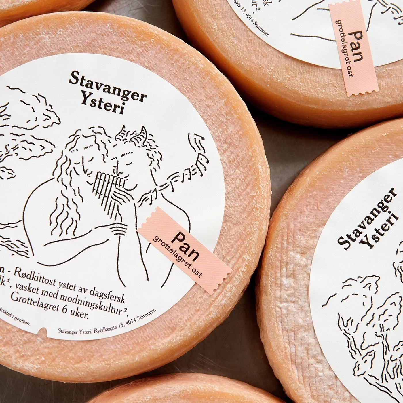 Varias ruedas de queso rosado vistas desde arriba, con etiquetas redondas blancas de Stavanger Ysteri y una tira rosa con el nombre «Pan»