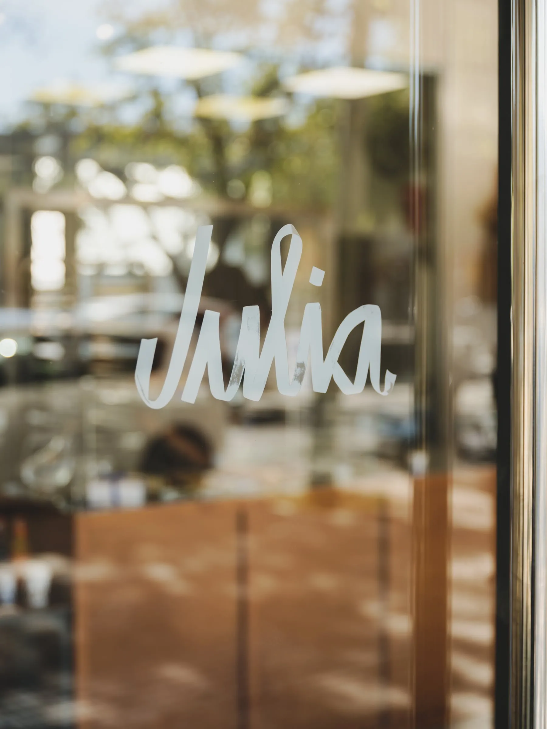 Logotipo de Julia en blanco sobre el cristal de la puerta de la cafetería, con las letras formadas por una cinta plegada y el interior desenfocado al fondo